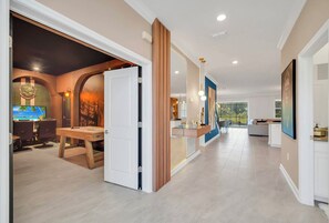 A spacious hallway with a dining area featuring a wooden table and chairs, a kitchen with modern appliances, and a large window providing a view of the outdoors. - 9BR house sleeps 24 with hot tub and pool (Kissimmee)