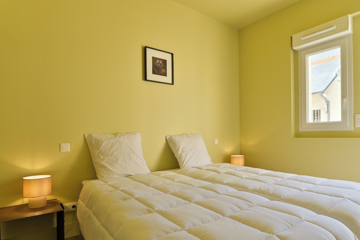 A bedroom with a bed, two bedside lamps, a framed picture on the wall, and a window.