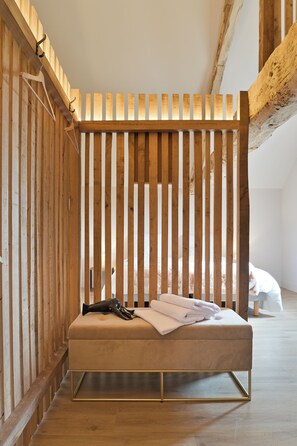 Habitación con separador de listones de madera, cama con colchón y almohadas, secador de pelo y una toalla doblada sobre la cama.