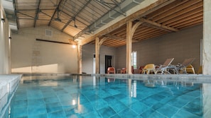 An indoor swimming pool with clear blue water, wooden beams, and lounge chairs.