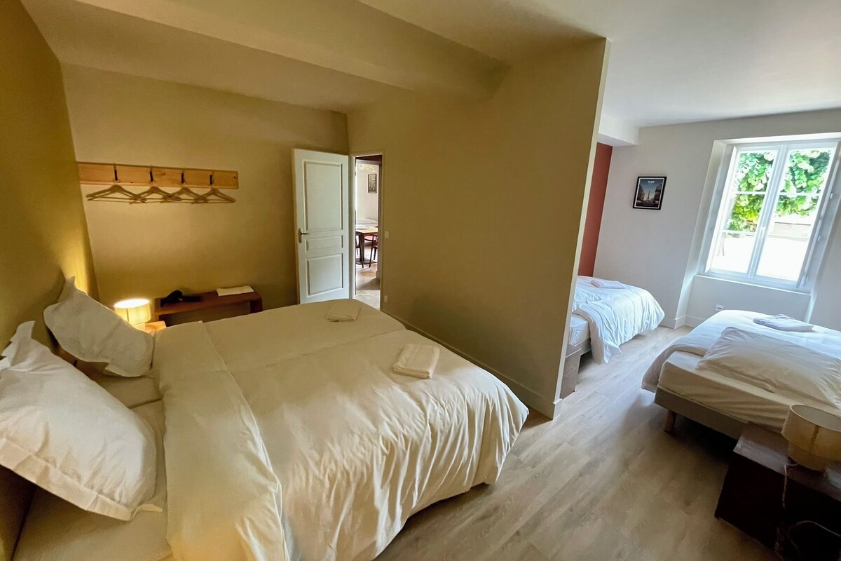 Habitación de hotel con una cama grande, dos camas más pequeñas, un escritorio con silla, armario y ventana con vistas.
