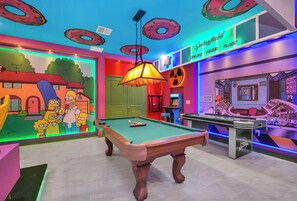 Une pièce lumineuse, avec une table de billard, une fresque murale représentant les personnages des « Simpsons » et un panneau indiquant  : « Centrale électrique de Springfield ».