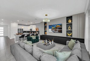 Ein modernes Wohnzimmer mit einem grauen Sofa, einem Couchtisch und einem Essbereich, im Hintergrund ist eine Küche zu sehen.