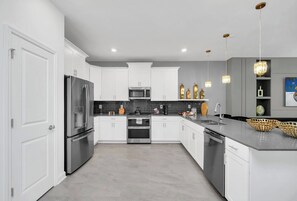 A modern kitchen with white cabinetry, stainless steel appliances, and a grey countertop. - Stunning 9BR Themed Villa | Immersive Experience (Davenport)