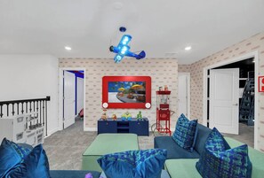A living room with a blue airplane decoration, a red wall-mounted TV, and a play kitchen set. - Stunning 9BR Themed Villa | Immersive Experience (Davenport)