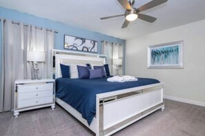 Una camera da letto con un letto, un comodino, una ventola a soffitto e un quadro appeso al muro.