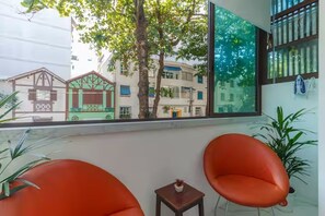 A room with two orange chairs, a small table with a plant, and a large window with a view of buildings. - Studio in Ipanema • Next to the Beach and Lagoon (Rio de Janeiro)