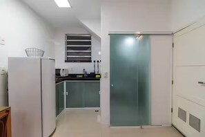 A modern kitchen with a refrigerator, a microwave, and a sink. There is a glass door leading to another room. - Studio in Ipanema • Next to the Beach and Lagoon (Rio de Janeiro)