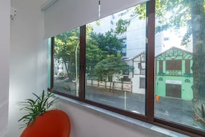 Une pièce avec une grande fenêtre, une plante et un fauteuil rouge.