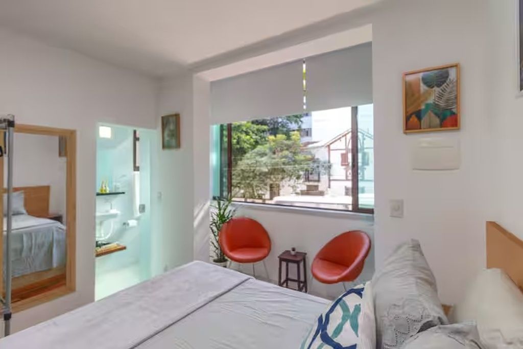 Une chambre d’hôtel avec un lit, une fenêtre donnant sur un beau paysage, une petite table et deux chaises rouges.