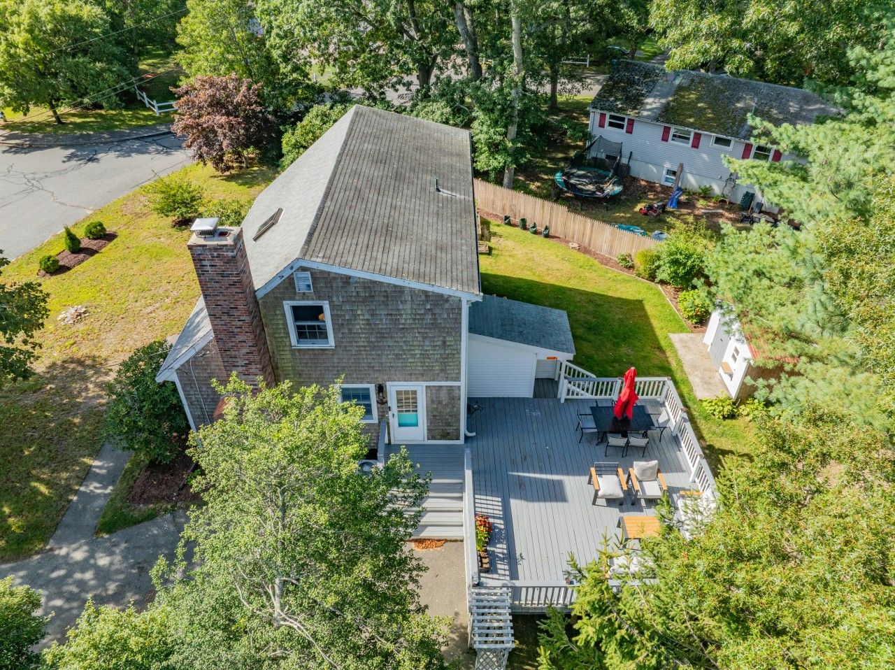 Ein zweistöckiges Haus mit einer Terrasse, einem Swimmingpool und einem eingezäunten Garten.