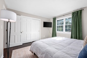 Een slaapkamer met een bed, een flatscreen televisie, een deur en een raam met gordijnen.