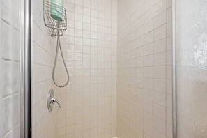 Een douchecabine met betegelde wanden, een handdouche en een bedieningskraan op de muur.