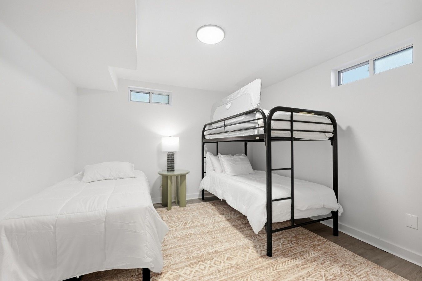 A room with bunk beds, a bedside table with a lamp, and a patterned rug.
