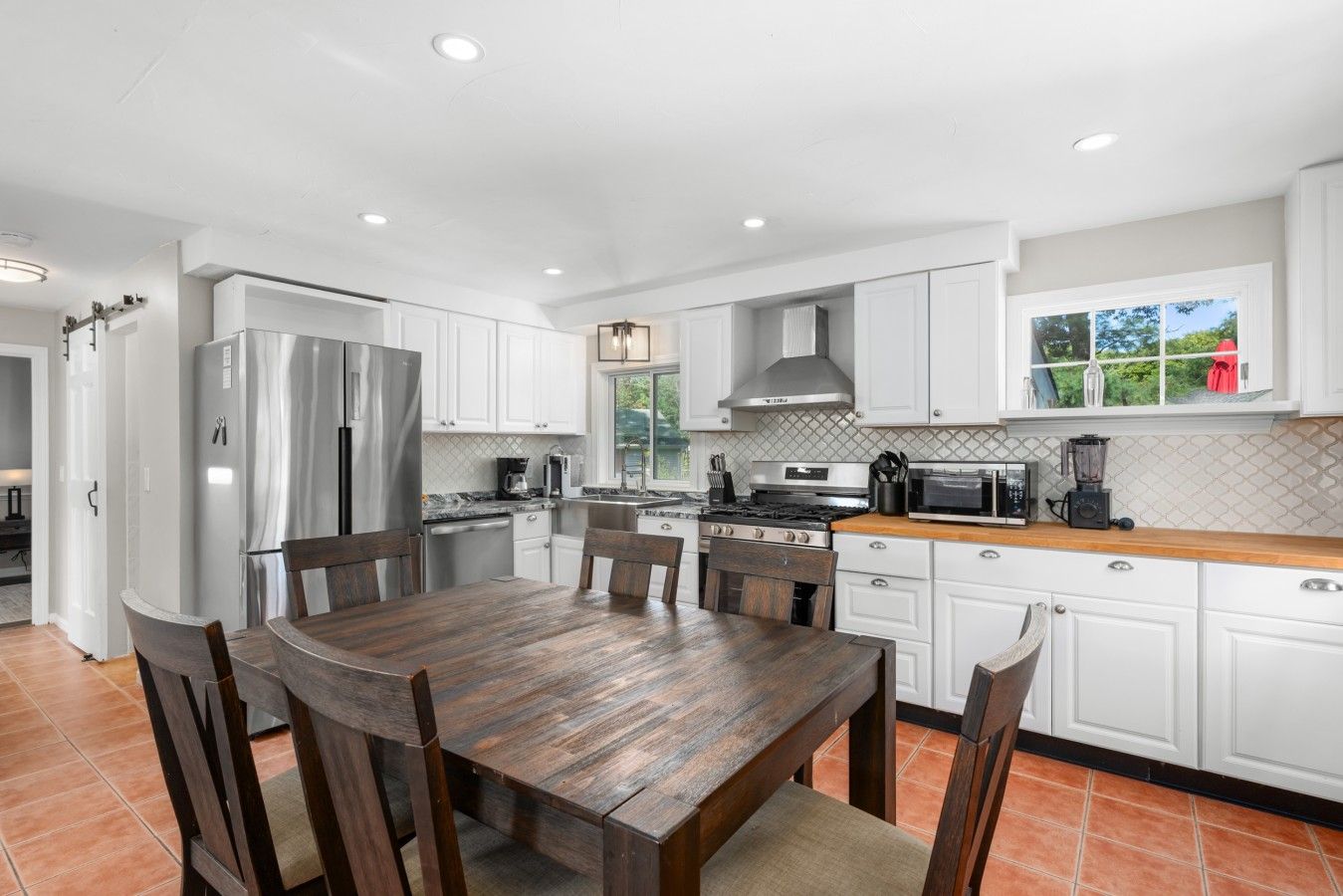 A modern kitchen with white cabinetry, a wooden dining table, and a large window.