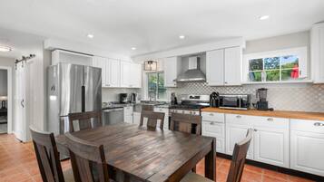A modern kitchen with white cabinetry, a wooden dining table, and a large window.