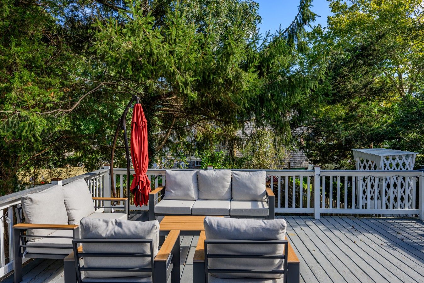 A deck with a sofa and chairs, a wooden table, and a red umbrella.