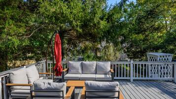 A deck with a sofa and chairs, a wooden table, and a red umbrella.