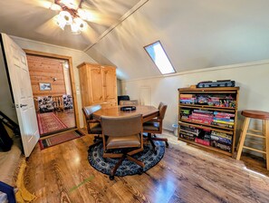 A room with a wooden dining table, chairs, a bookshelf with board games, a ceiling fan, and a skylight. - Family & Dog Friendly Pollock Pines Cabin near Jenkinson Lake & Tahoe (Pollock Pines)