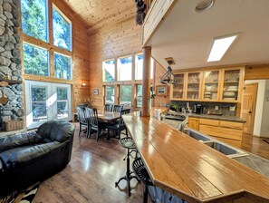 A spacious kitchen with wooden cabinets, a large island, and a dining area with chairs. - Family & Dog Friendly Pollock Pines Cabin near Jenkinson Lake & Tahoe (Pollock Pines)