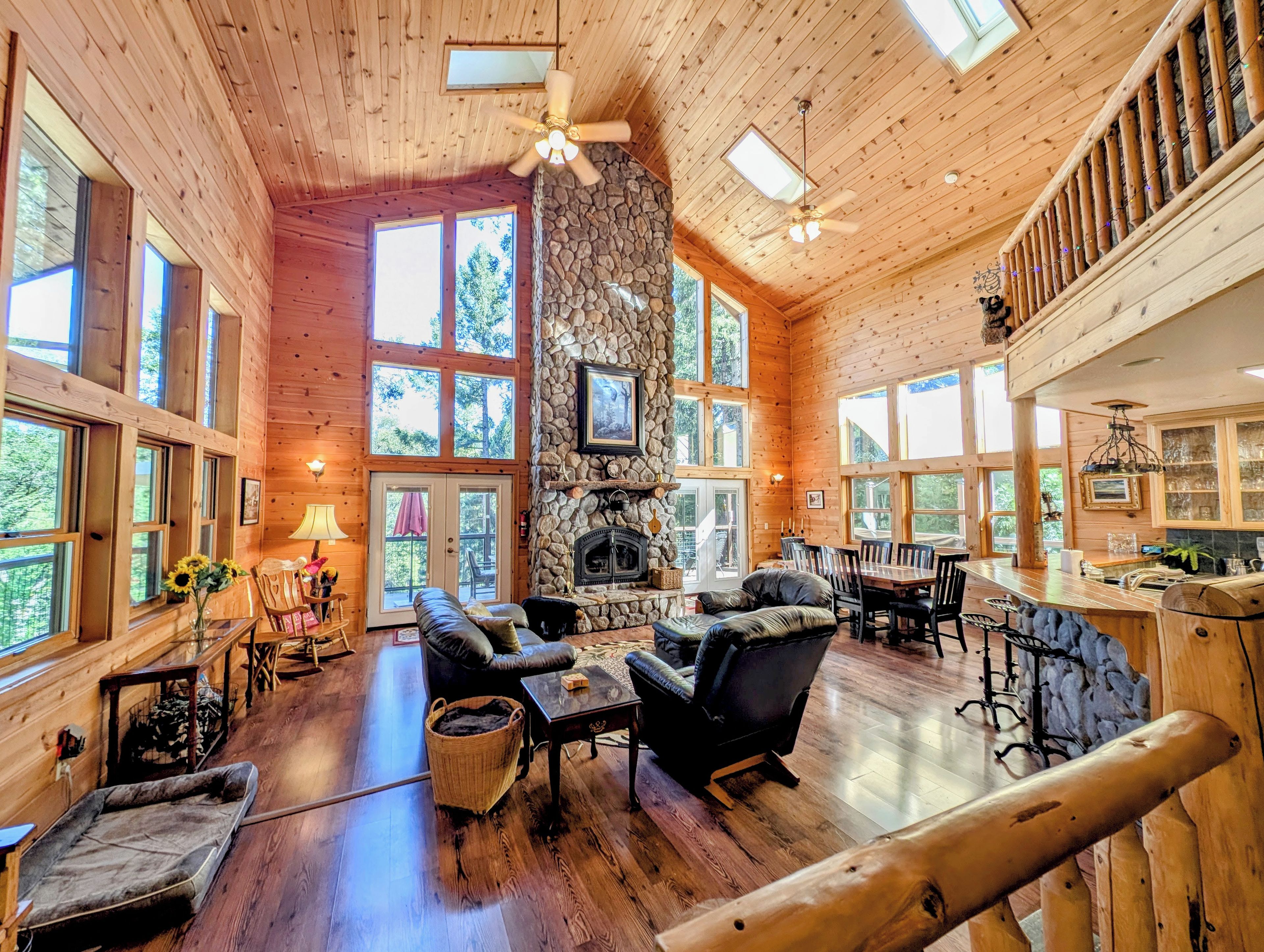 A spacious lodge with a stone fireplace, wooden floors, and large windows offering views of the outdoors.