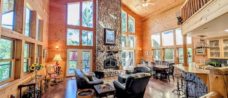 A spacious lodge with a stone fireplace, wooden floors, and large windows offering views of the outdoors.