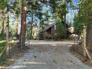 A rustic cabin surrounded by a gravel path and metal gates, with a forested backdrop. - Family & Dog Friendly Pollock Pines Cabin near Jenkinson Lake & Tahoe (Pollock Pines)