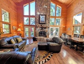 A log cabin interior with a stone fireplace, leather furniture, and large windows. - Family & Dog Friendly Pollock Pines Cabin near Jenkinson Lake & Tahoe (Pollock Pines)