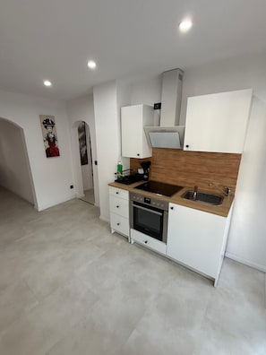 A compact kitchen with white cabinetry, a wooden countertop, a built-in oven, and a sink.