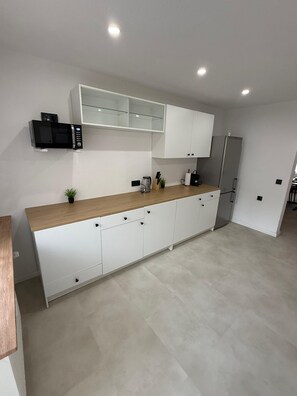 A modern kitchen with white cabinets, a microwave, a refrigerator, and a wooden countertop.
