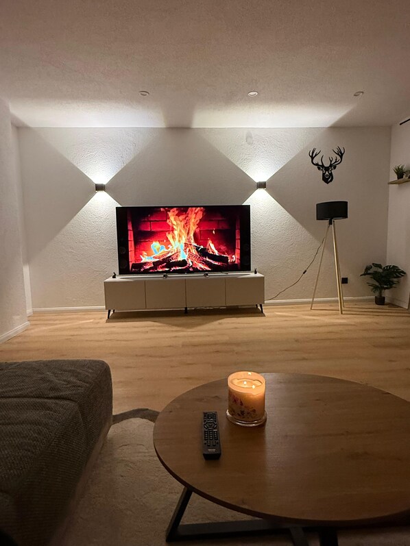 A living room with a flat-screen TV, a wooden coffee table with a candle, and a remote control.