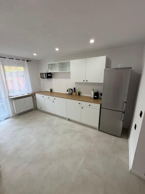 A modern kitchen with white cabinets, a stainless steel refrigerator, and a wooden countertop.