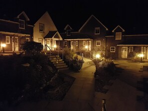 A residential building with multiple entry points, a central staircase, and a well-lit pathway leading to the entrance. - 6 Cara Anan- 2 Bedroom House (Stirling)