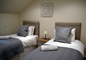A hotel room with two beds, each with a headboard, a bedside table with a lamp, and a decorative wall piece. - 6 Cara Anan- 2 Bedroom House (Stirling)