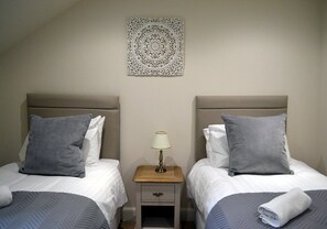 A hotel room with two beds, a nightstand with a lamp, and a decorative wall piece. - 6 Cara Anan- 2 Bedroom House (Stirling)