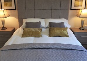 A neatly made bed with a grey quilt, two pillows, and two bedside lamps. - 12 Alainn Eve - 2 Bedroom House, Killin (Stirling)