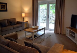 Una sala de estar con sofá, mesa de centro, mueble para televisión y puerta corrediza de vidrio que da a un área exterior.