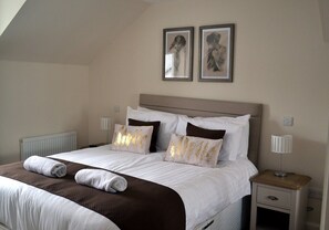 A neatly made bed with white and brown bedding, two bedside lamps, and two framed pictures on the wall. - 3 Dorcha's Mian - 2 Bedroom House, Killin (Stirling)