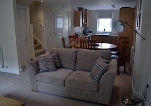A living room with a sofa, a dining table, and chairs. There is a kitchen area with cabinets and a microwave. A staircase is visible in the background. - 3 Dorcha's Mian - 2 Bedroom House, Killin (Stirling)