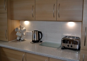 A kitchen with wooden cabinets, a kettle, a toaster, and a mug holder. - 3 Dorcha's Mian - 2 Bedroom House, Killin (Stirling)