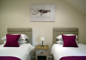 A hotel room with two beds, each with a headboard, a bedside table with a lamp, and a single artwork on the wall. - 9 Inverfinn - 2 Bedroom House Killin (Stirling)