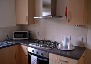 A kitchen with a gas stove, microwave, and stainless steel range hood. - Orangewood House (4) - 2 Bedroom House, Killin (Stirling)