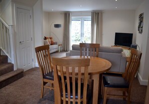 A living room with a round wooden table, two chairs, a sofa, a television, and a staircase. - Orangewood House (4) - 2 Bedroom House, Killin (Stirling)