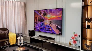 Un salon moderne avec un téléviseur à écran plat fixé au mur, une table basse sur laquelle est posé un jeu d’échecs, un canapé et une étagère décorative agrémentée de plantes.