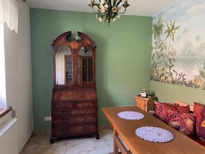 A room with a wooden dresser, a dining table with placemats, a sofa with patterned cushions, and a mural of a tropical landscape. - NEW! Elbenau Vacation Home (Elbenau)