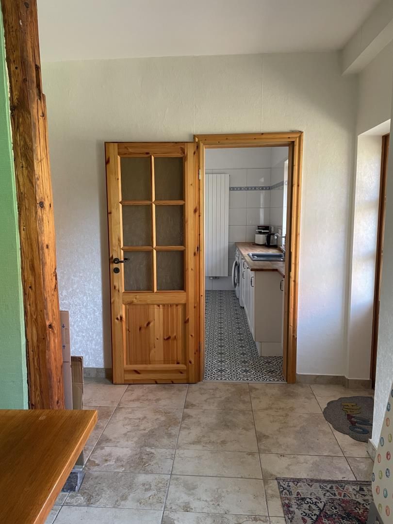 Ein Flur, der zu einer Küche mit Holztür, Fliesenboden und einer Bank führt.