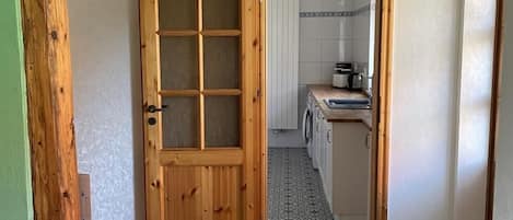 A hallway leading to a kitchen with a wooden door, tiled floor, and a bench.