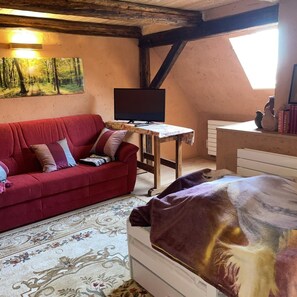 A cozy room with a red sofa, a flat-screen TV, a small table, and a bed with a blanket. - NEW! Elbenau Vacation Home (Elbenau)