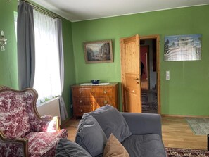 A room with a green wall, a wooden cabinet, a sofa, a chair, and two paintings. - NEW! Elbenau Vacation Home (Elbenau)