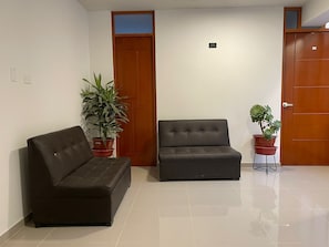 A room with a sofa, two potted plants, a door, and a tiled floor. - Hotel Paucartambo Piedra grandre Lodge (Paucartambo)